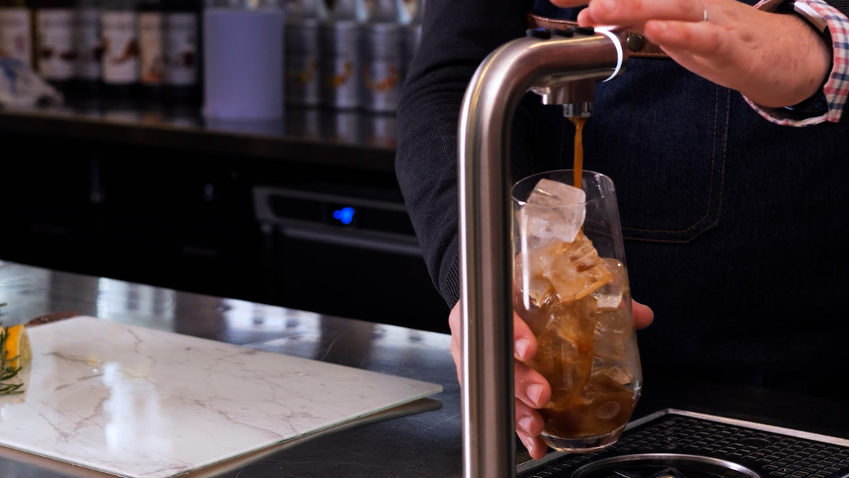 Cold coffee pouring from a POUR'D font into a glass of ice