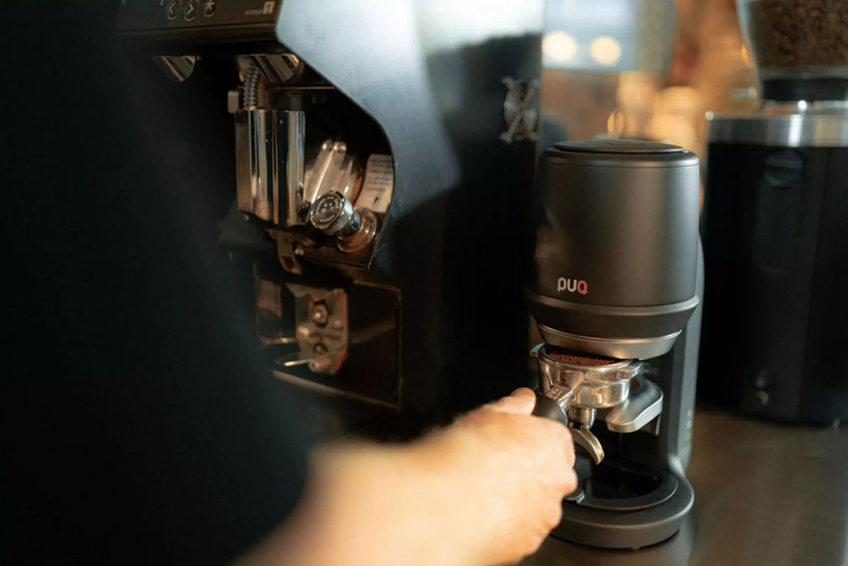 Barista sliding a portafilter into a black PUQ Press beside the grinder